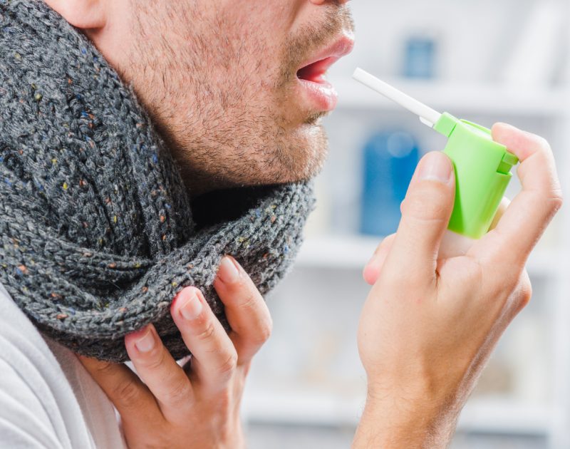 Man in scarf with sore throat spraying throat medicine